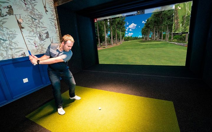 Home golf simulator room with hitting mat, enclosure and projected fairway