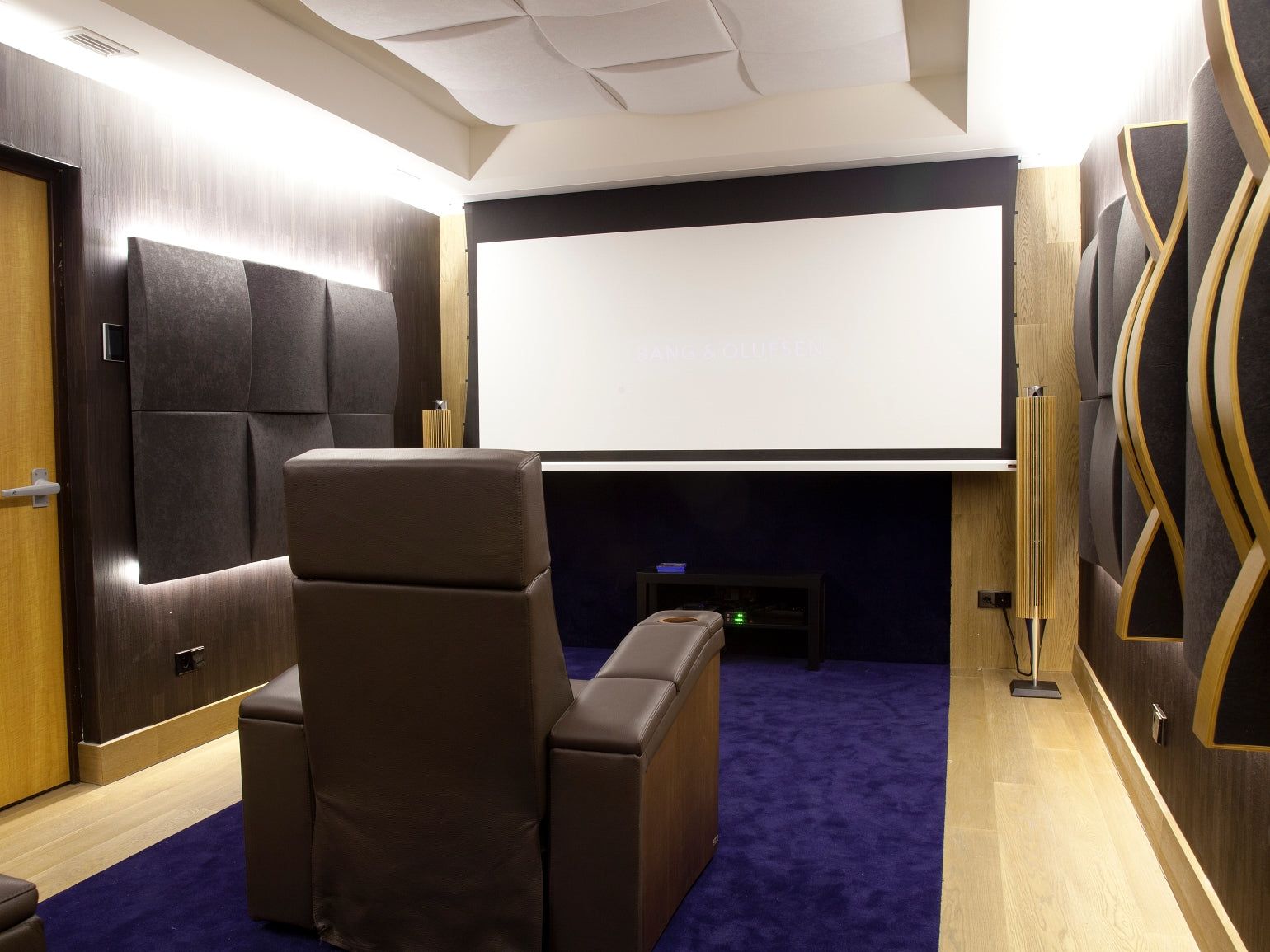 Home theatre with Vicoustic fabric panels and wood diffusers beside the screen and leather recliners