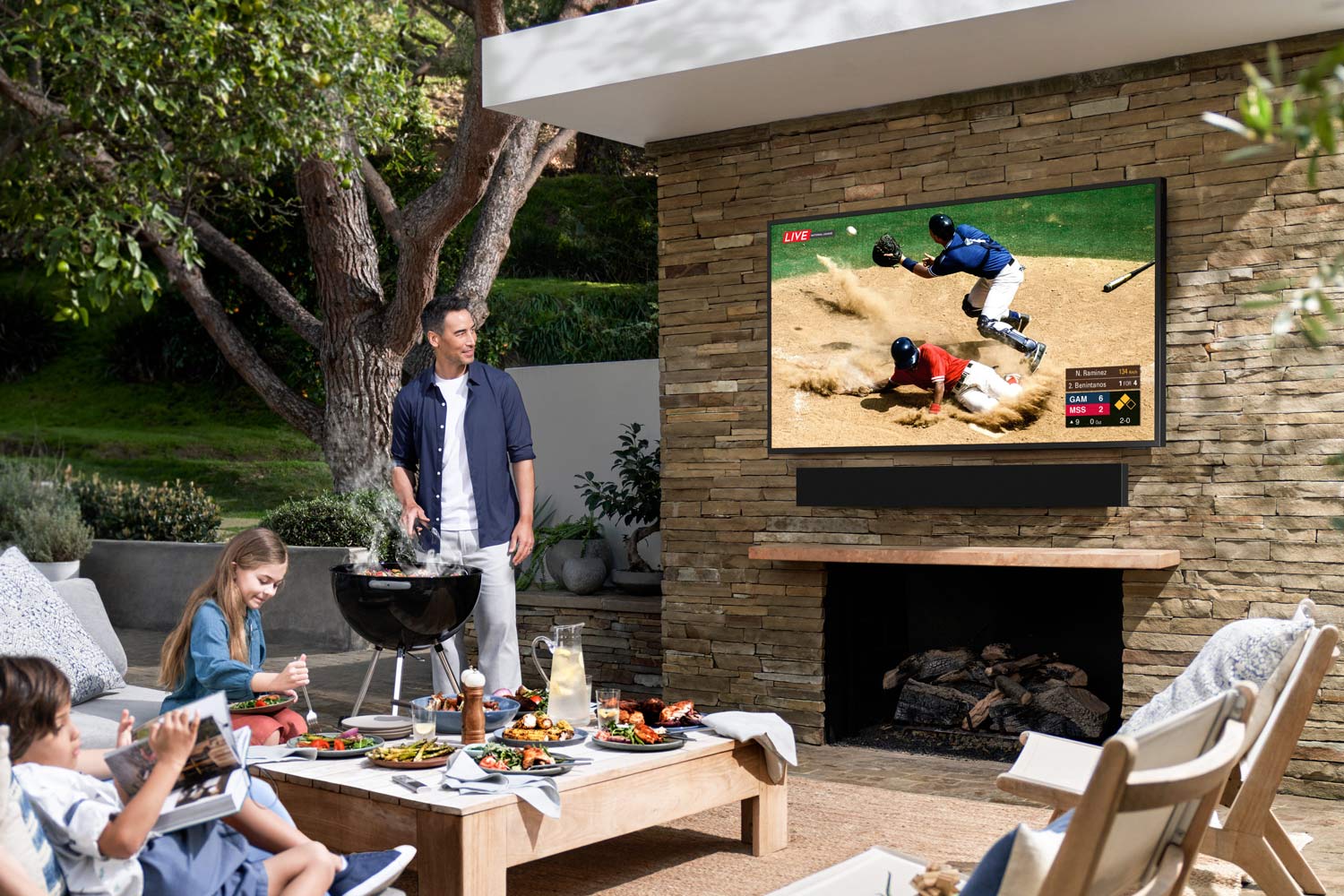 Family barbecuing while watching a Samsung The Terrace outdoor TV