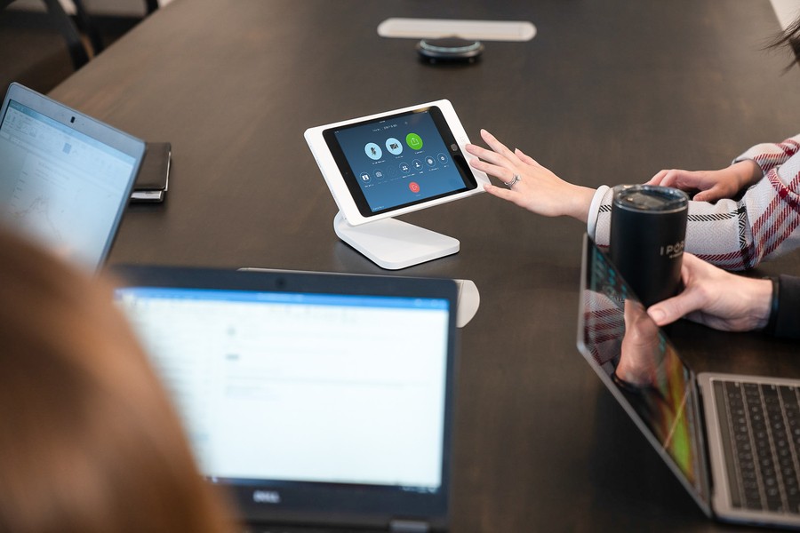 A woman pressing a touch screen depicting AV controls for a meeting room.